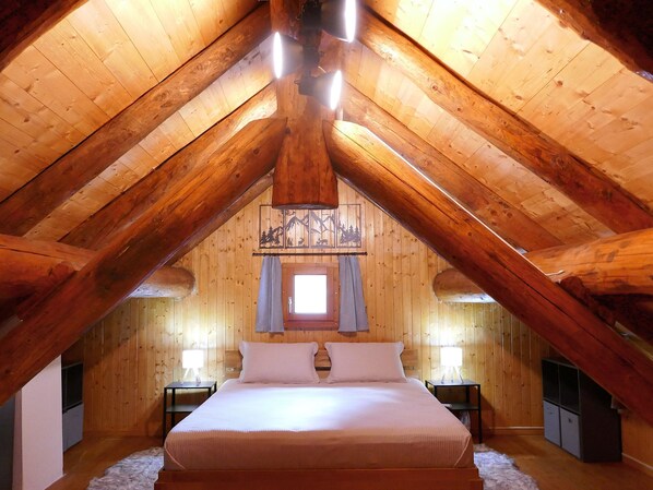 A high-ceilinged attic bedroom with a large bed, two bedside tables, and a window with curtains. - Rustico Grace by Interhome (Malvaglia)