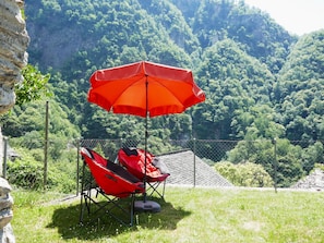 A red umbrella and two red chairs in a grassy area with a mountainous backdrop. - Rustico Grace by Interhome (Malvaglia)