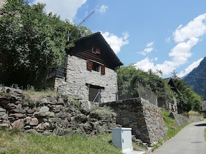 A stone house with a sloped roof, a small window with shutters, and a stone wall in front. - Rustico Grace by Interhome (Malvaglia)
