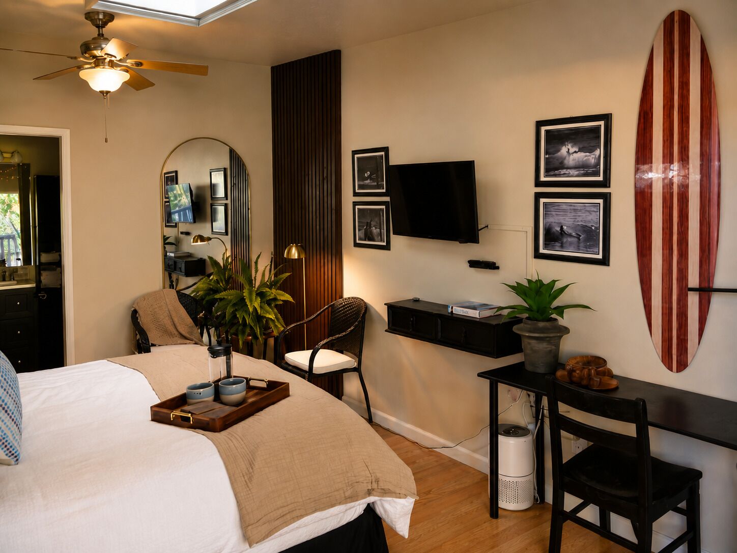 A bedroom with a bed, a desk, a chair, a TV, a surfboard, and a ceiling fan.