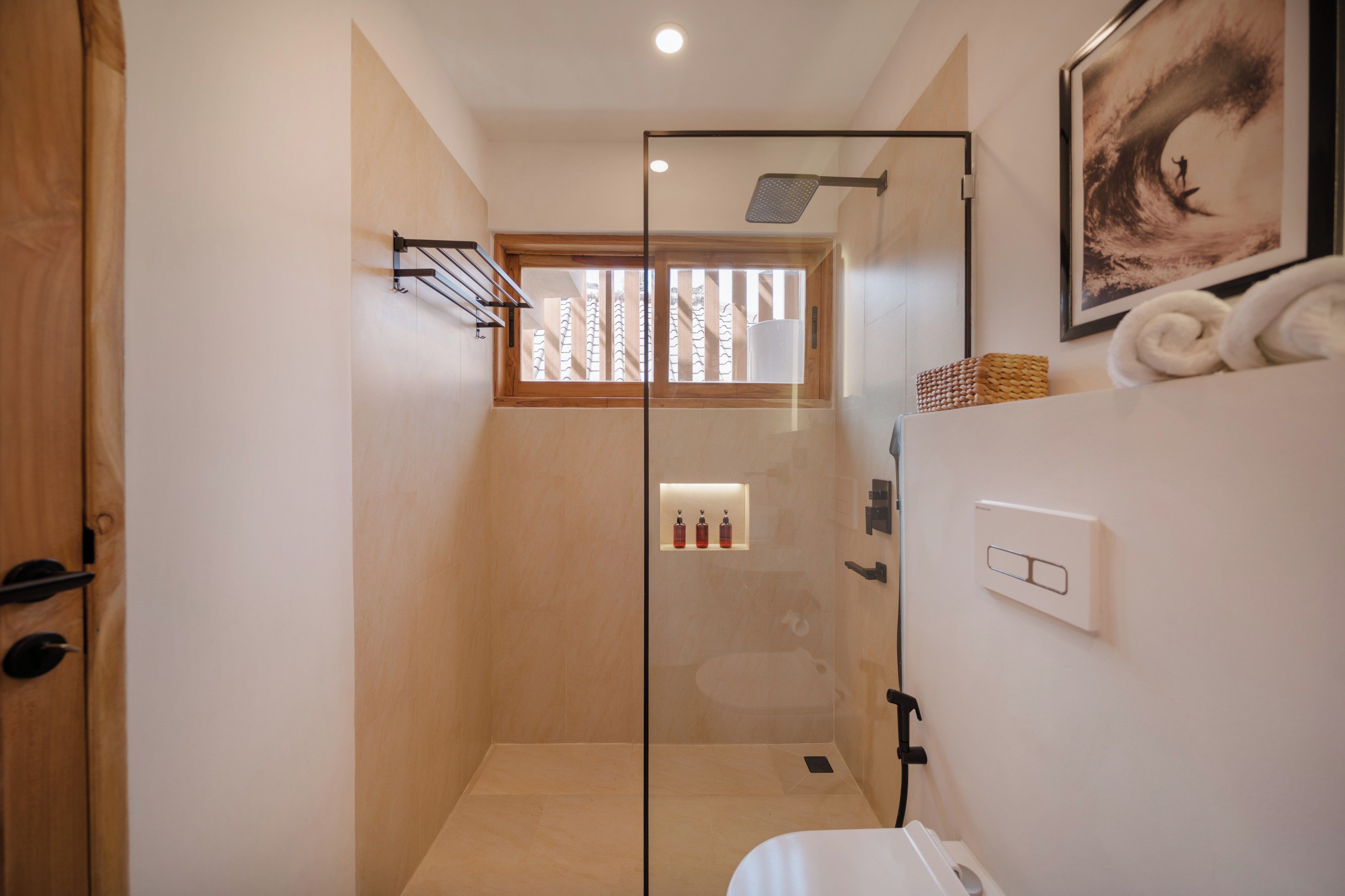 A modern bathroom with a glass shower enclosure, a wooden door, and a towel rack.