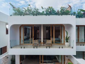 A modern building with a glass balcony, wooden furniture, and potted plants. - Cadaques Villa by Betterplace (Ungasan)