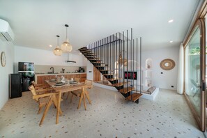 Une cuisine moderne avec des meubles en bois, une table à manger pour quatre personnes et un escalier doté d’une rampe en métal.