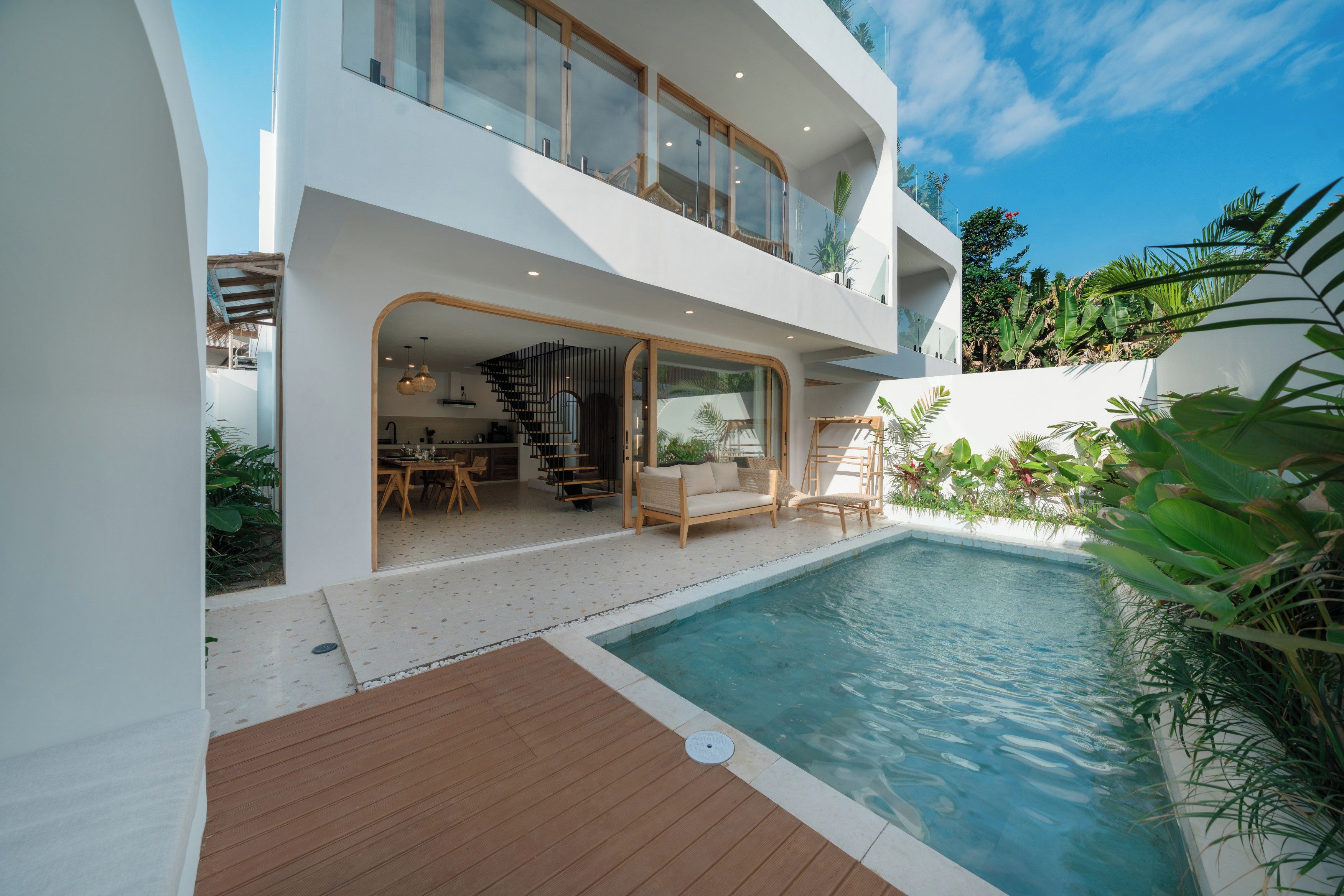 Et moderne hus med to etager, en pool, udendørs møbler og et spiseområde.