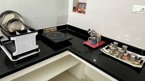 Et køkken med en sort bordplade, et hvidt flisebordsplade, en sort induktionskogetop og en bakke med røde og hvide elementer samt køkkenredskaber.