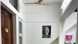 En gang med ventilator i loftet, en trædør og en hvid væg med et indrammet billede.