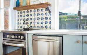 Ett kök med en ugn och diskmaskin i rostfritt stål, samt ett fönster med utsikt över grönområden.