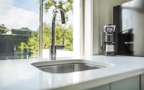 Ett modernt kök med en diskho i rostfritt stål, en kaffebryggare och ett fönster med utsikt över grönområden.