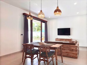 Een moderne eetruimte met een houten tafel en stoelen, een flatscreen televisie aan de muur en een groot raam met gordijnen.