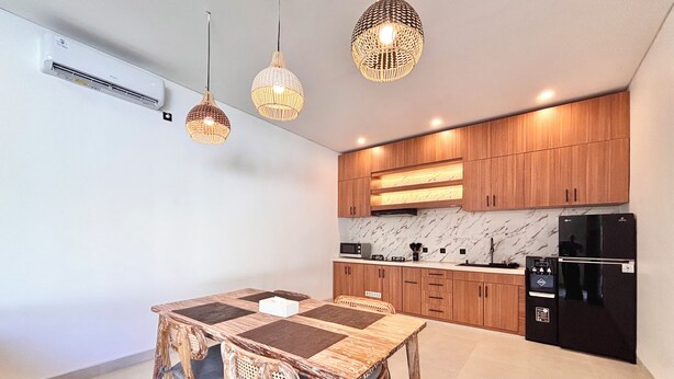 A modern kitchen with wooden cabinets, a black refrigerator, and a dining area with a wooden table and chairs. - Private Two Bedroom Pool Villa, Spacious Garden and Tranquil (Ubud)