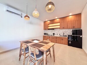 Een moderne keuken met houten kasten, een zwarte koelkast, en een eethoek met een houten tafel en stoelen.
