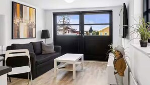 Ett modernt vardagsrum med en svart soffa, ett vitt soffbord och en tavla på väggen.