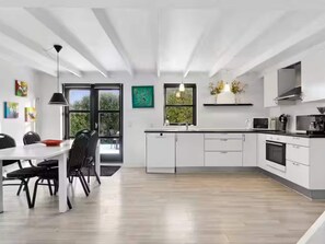 Eine moderne Küche mit weißen Schränken, ein Essbereich mit Tisch und Stühlen sowie ein großes Fenster für natürliches Licht.