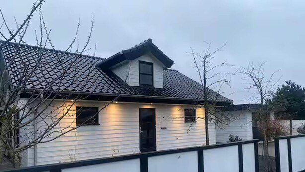 Ett envåningshus med ett tak täckt av tegelpannor, en vit fasad och en dörr med svart ram.