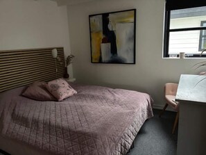 Ein Schlafzimmer mit einem Bett, einem Sessel, einem Gemälde und einem Fenster.