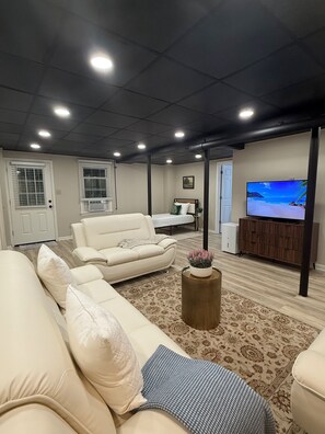 A living room with a sectional sofa, a coffee table, a flat-screen TV, and a fireplace. - The Modern Garden Suite: With Private Entrance ~ 1 BR - sleeps 3 (Manchester)