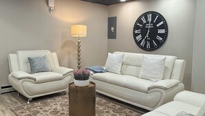 Ein modernes Wohnzimmer mit einem Ecksofa, einer runden Wanduhr und einem gemusterten Teppich.