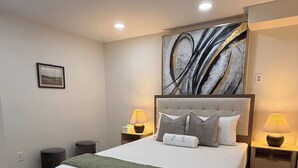 Ein Schlafzimmer mit einem großen Bett, zwei Nachttischen, einem Wandbild und einem gemusterten Teppich.