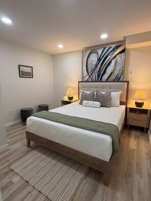Ein Schlafzimmer mit einem großen Bett, zwei Nachttischen, einem Wandbild und einem gemusterten Teppich.