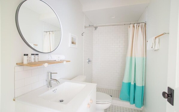 Ein modernes Badezimmer mit Waschbecken, Spiegel und Dusche in Weiß.