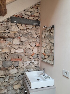 A bathroom with a stone wall, a white sink, and a mirror. - 102 - Music Room (Belluno)