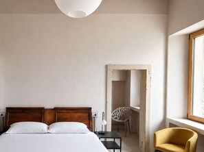 A bedroom with a bed, bedside table, lamp, chair, and a window. - 102 - Music Room (Belluno)