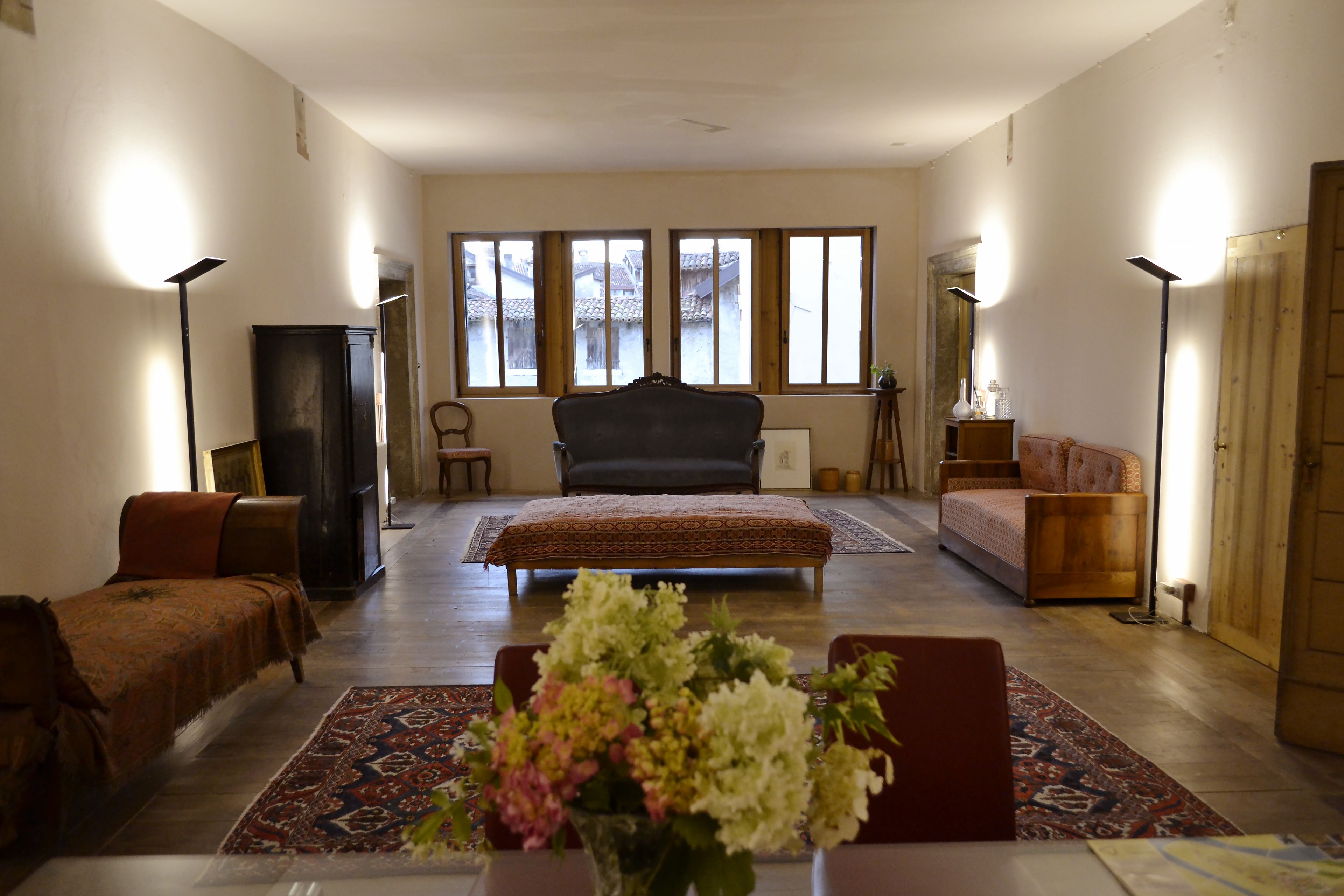 A spacious room with a large bed, a sofa, a chair, and a table with a vase of flowers.