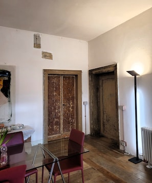 Una habitación con una mesa de vidrio, sillas rojas, una puerta de madera y una lámpara de pie.