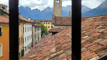 Blick durch ein Fenster auf eine Stadt mit Terrakotta-Dächern, einen Turm und Berge im Hintergrund.