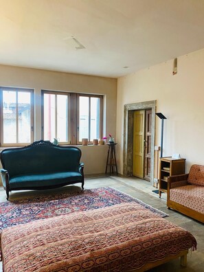 A room with a large bed, a sofa, a small table, and a window with curtains. - 105 - Room of Books (Belluno)