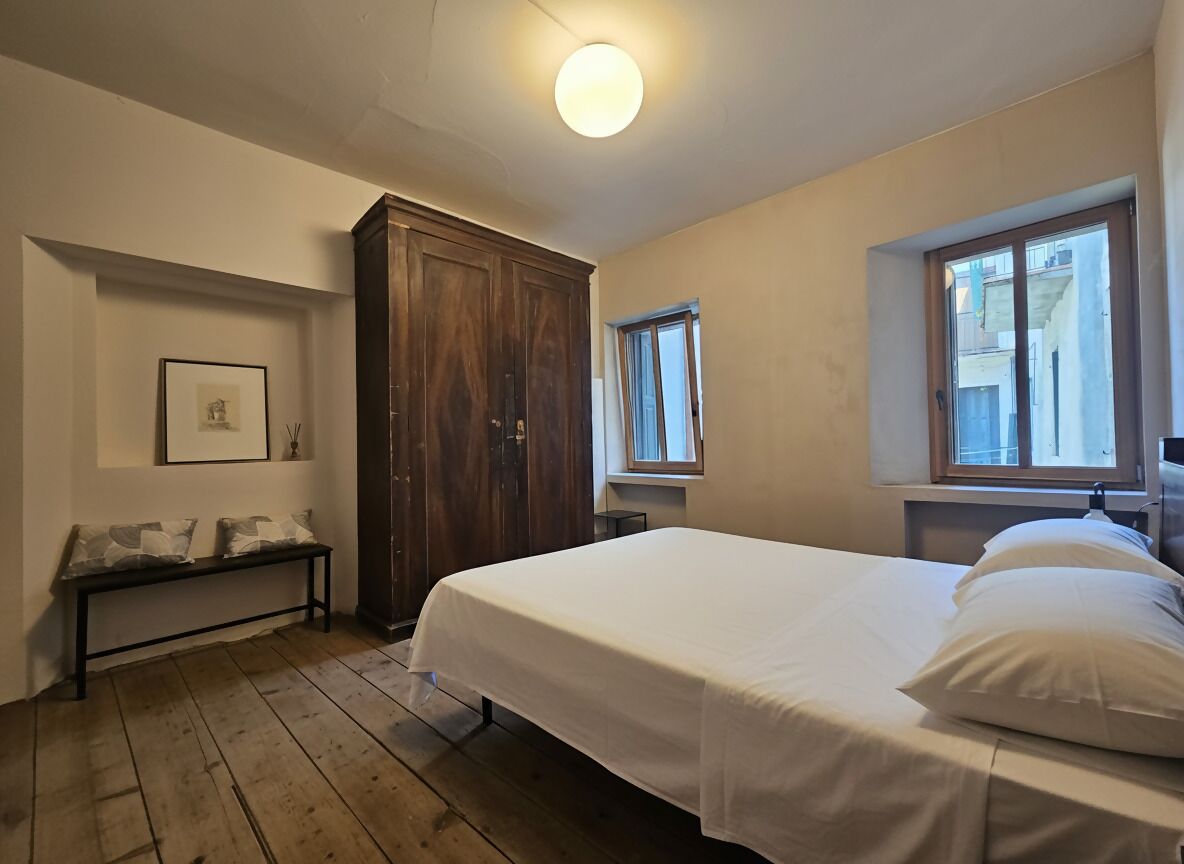 Un dormitorio con cama, armario de madera, banco y ventana.
