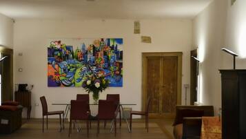 Uma sala de jantar com mesa e cadeiras, um quadro grande e colorido na parede, e uma porta de madeira.