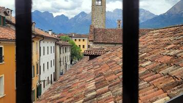 A view of terracotta-tiled rooftops, a stone tower, and mountains in the background.