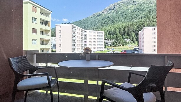 Un balcón con dos sillas y una mesa, con vistas a una montaña y edificios.