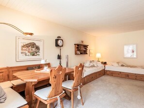 A cozy room with a wooden dining table, chairs, a bed, a bedside table with a lamp, and a wall clock. - Skyline Apartment 203 on Lake St. Moritz by Interhome (St. Moritz)