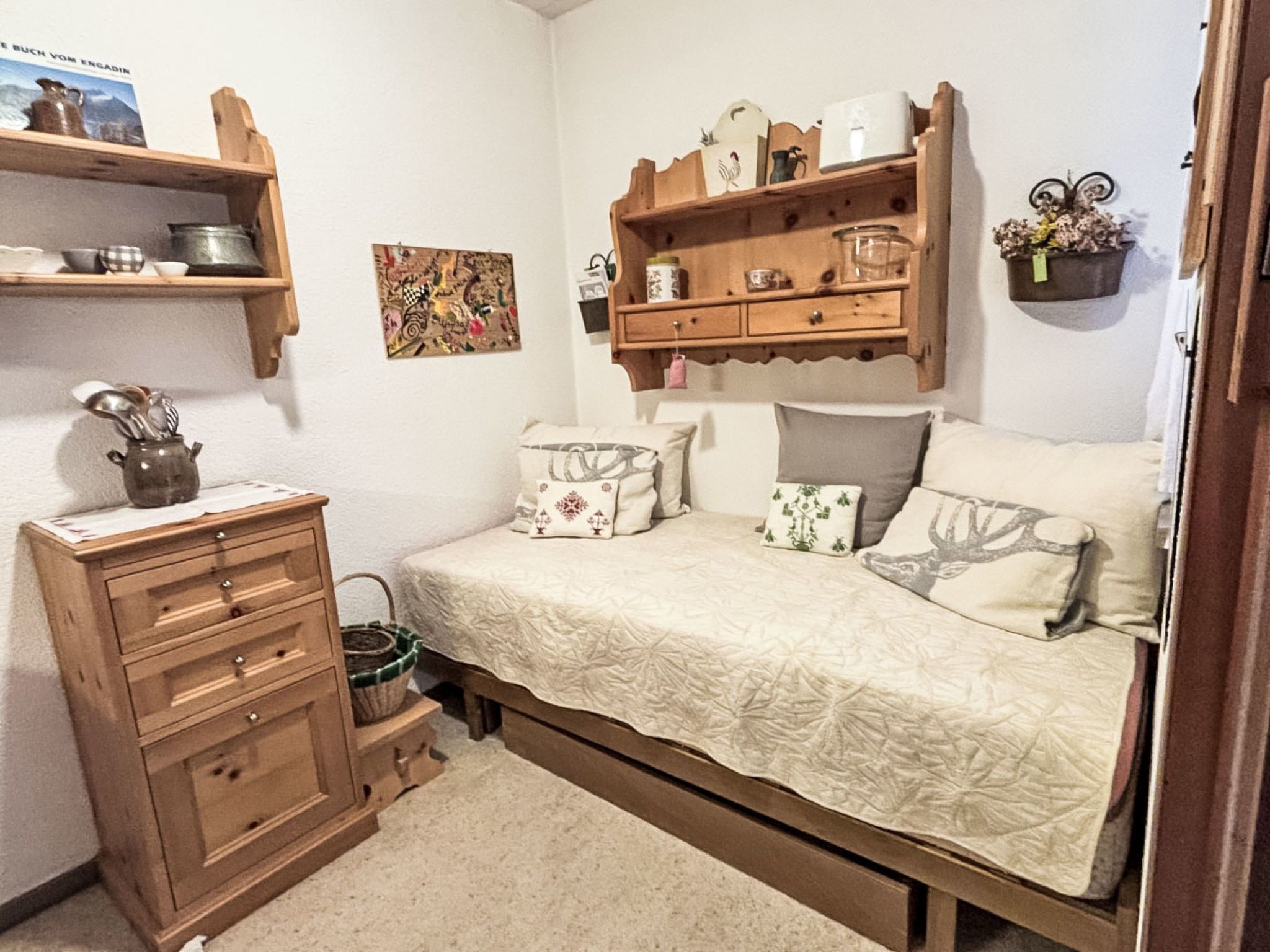 A bedroom with a bed, a dresser, shelves with various items, and a wall-mounted picture.