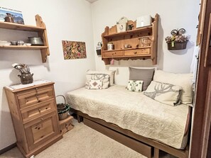 Ein Schlafzimmer mit einem Bett, einem Schminktisch, Regalen mit diversen Gegenständen und einem an der Wand hängenden Bild.