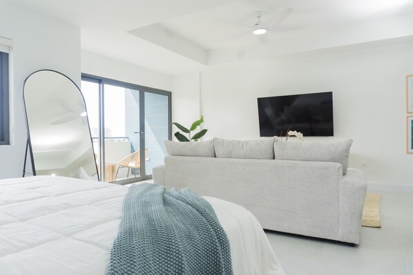 Un dormitorio moderno con una cama grande, un sofá gris, un televisor de pantalla plana y un balcón con vistas.