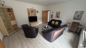 Uma sala de estar com sofá, mesa de centro, televisão e estante de livros.