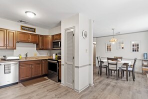 A modern kitchen with wooden cabinets, stainless steel appliances, and a dining area with a table and chairs. - 3BR Home @ Camp Hill Close to Hershey & Harrisburg (Camp Hill)