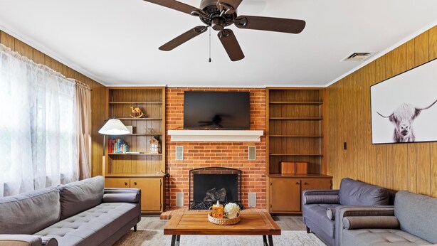 Una sala de estar con chimenea, dos sofás, una mesa de centro y un ventilador de techo.