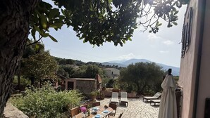 An outdoor patio with stone flooring, a round wooden table, and several chairs. - Villa Le Cicale in Procchio (Marciana)