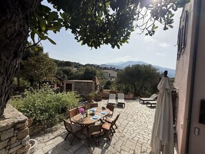 Eine Terrasse im Freien mit Steinböden, einem runden Holztisch und mehreren Stühlen.