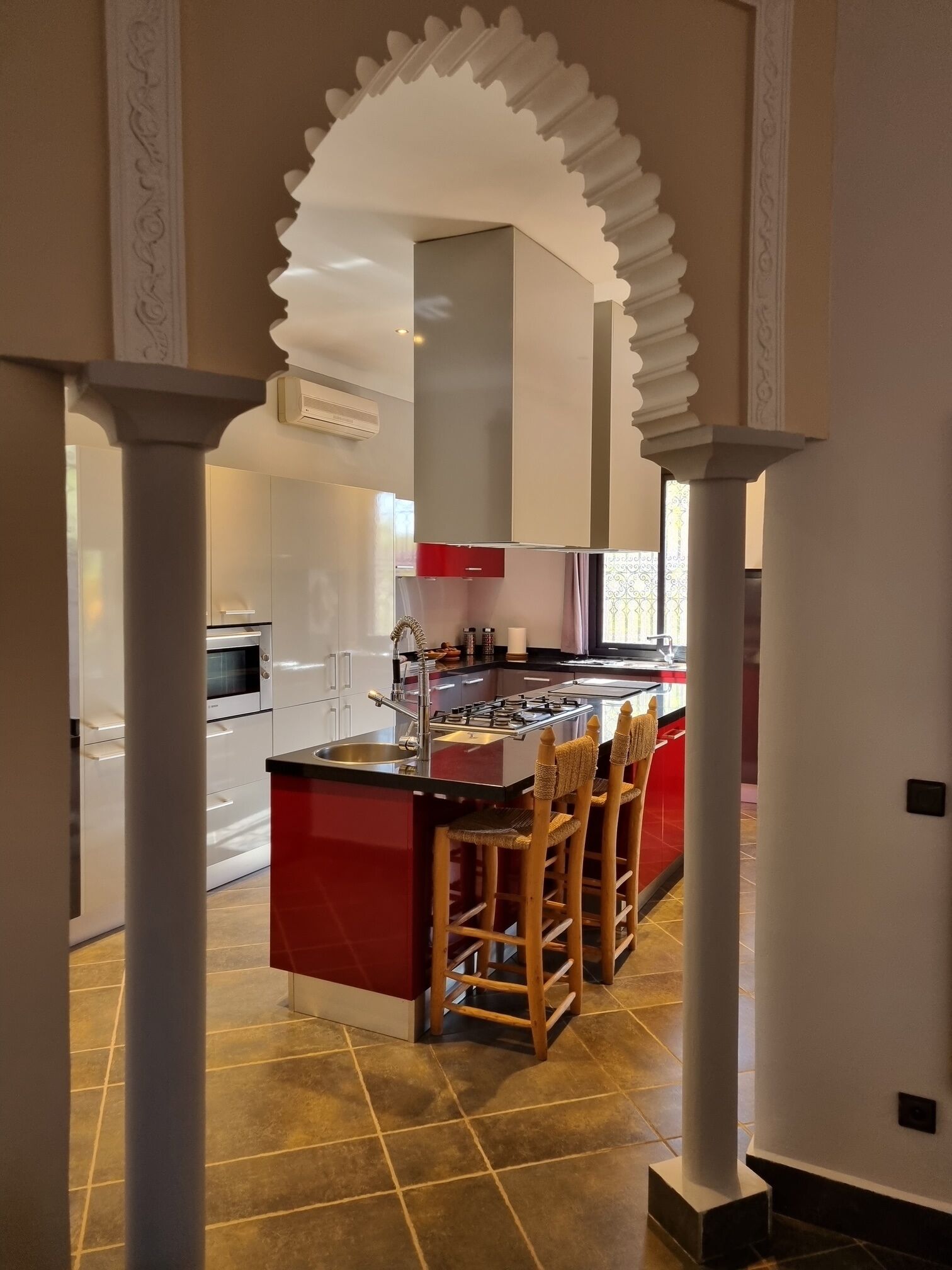 A modern kitchen with a central island, bar stools, and a view into the dining area.