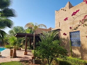 A courtyard with a pool, palm trees, and a building with a blue decorative window. - Villa with a huge private pool, 15 minutes from Marrakech (Douar Erragueb / Marrakech)