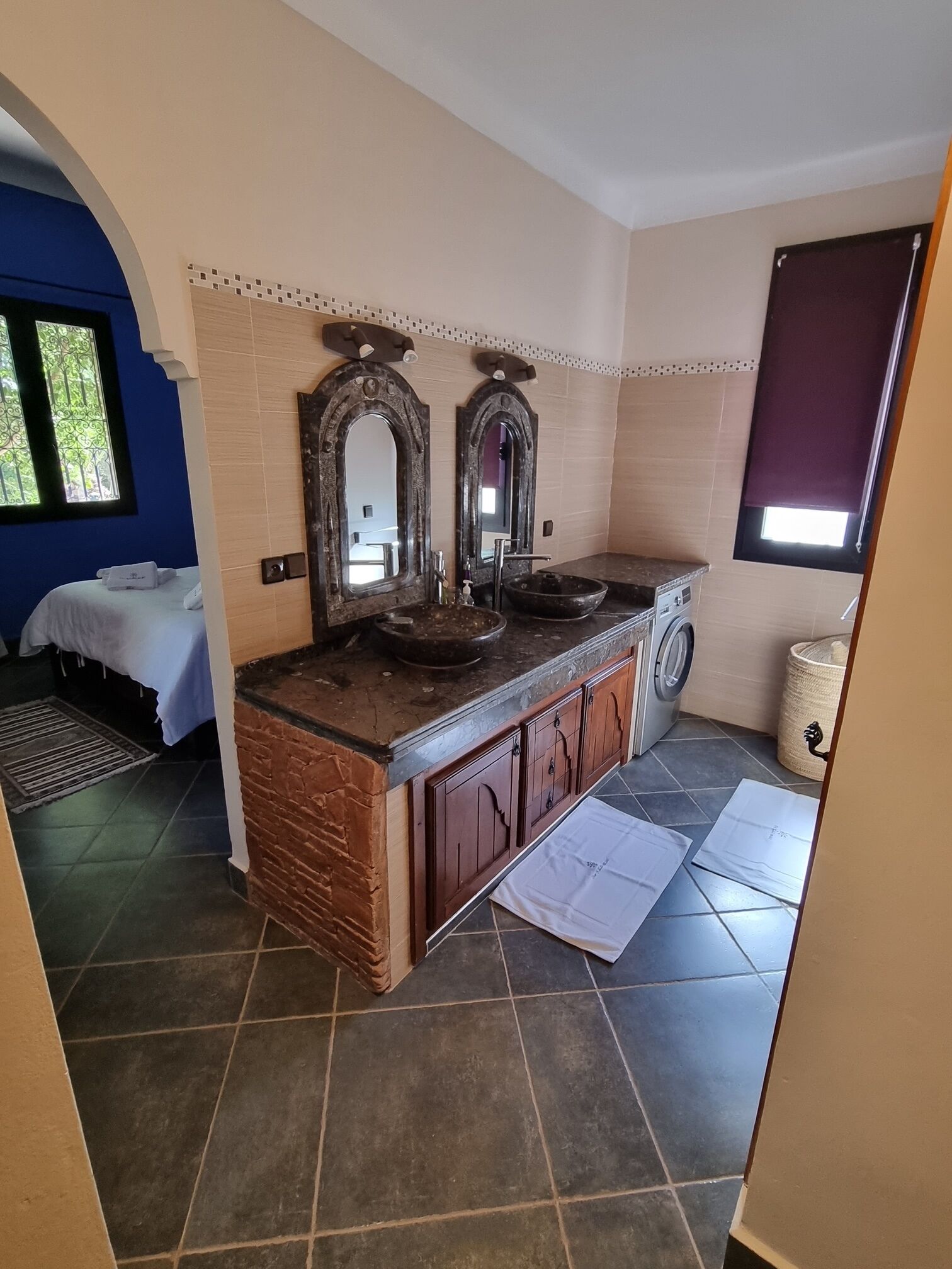 A bathroom with a sink, two mirrors, a washing machine, and a window.
