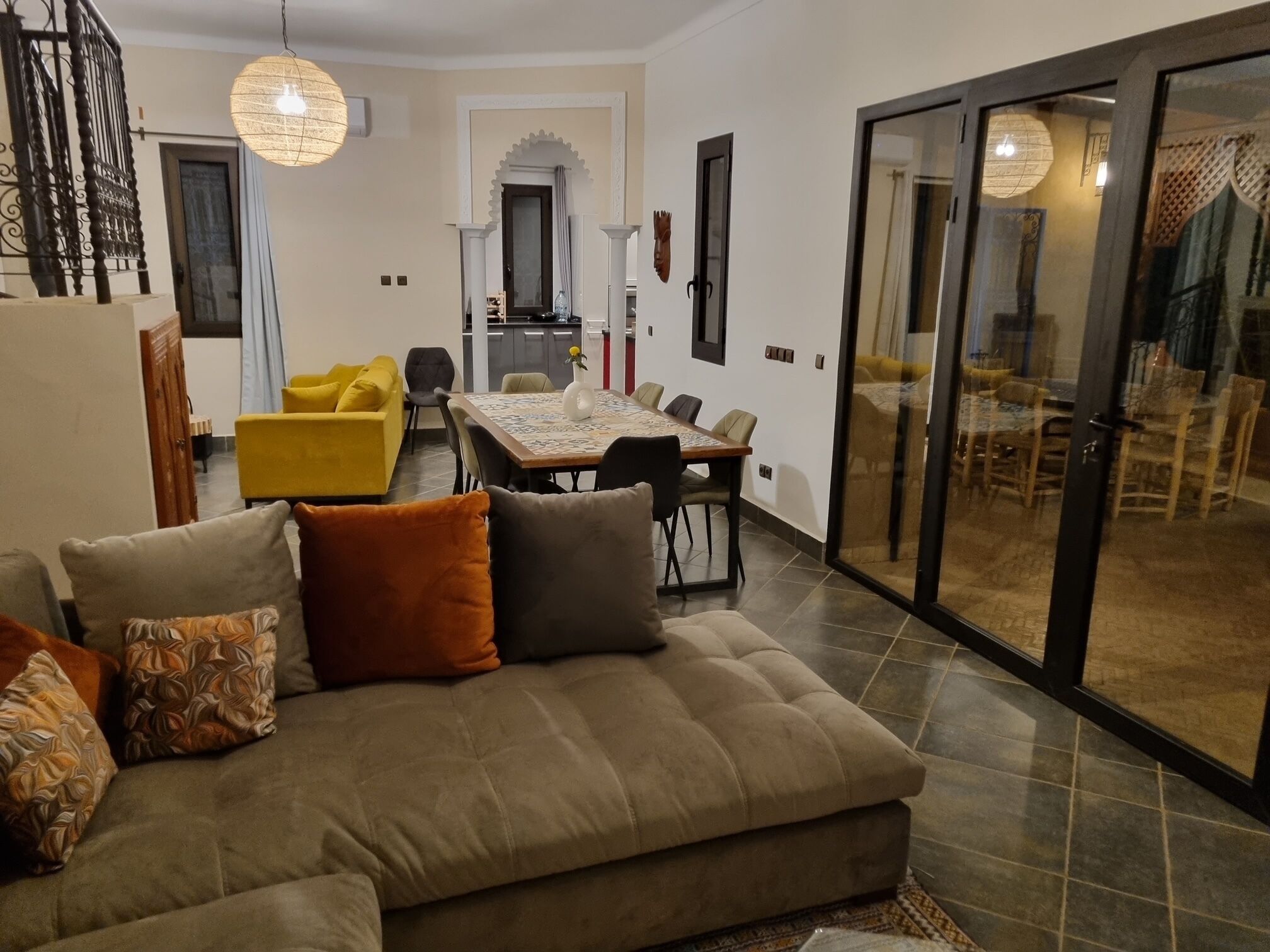 A living room with a sofa, a dining table, and chairs. There is a staircase leading to an upper level.