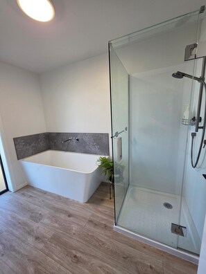 A modern bathroom with a glass-enclosed shower, a freestanding bathtub, and a wooden floor.