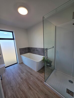 Une salle de bain moderne avec une douche à l’italienne, une baignoire sur pieds et un plancher en bois.