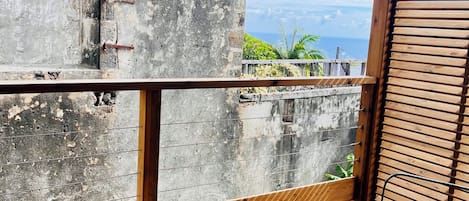 Eine Holzterrasse mit Tisch und Stühlen, mit Blick auf eine Küstenlandschaft und das Meer, umgeben von Vegetation.